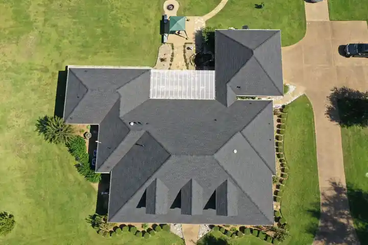 Overhead drone view of a finished dark hip roof with three dormers, set in a green lawn
