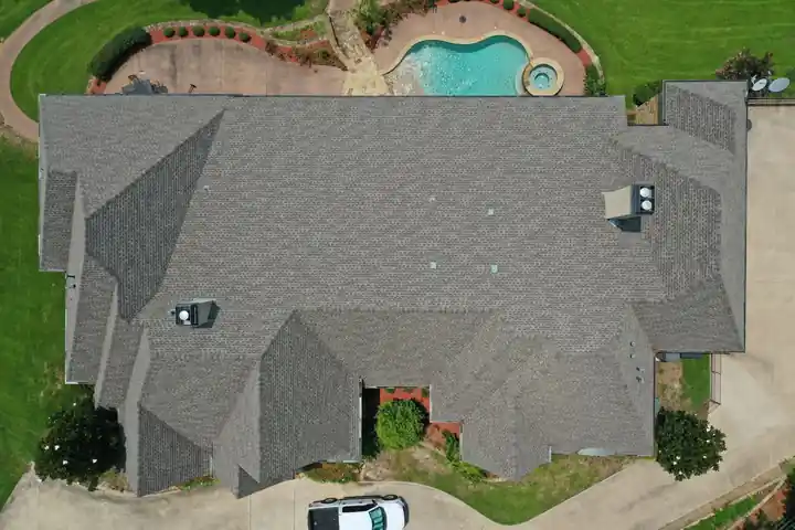 Top-down view of a grey shingle roof beside a kidney-shaped pool and lawn