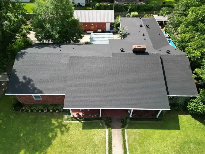 Top-down view of a red-brick ranch house roof on a green lawn