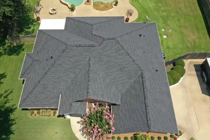 Overhead drone view of a large charcoal shingle roof with many hips and valleys, a pool behind it