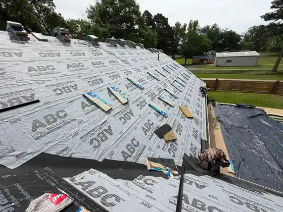 A roofer laying underlayment with shingle bundles staged beside him