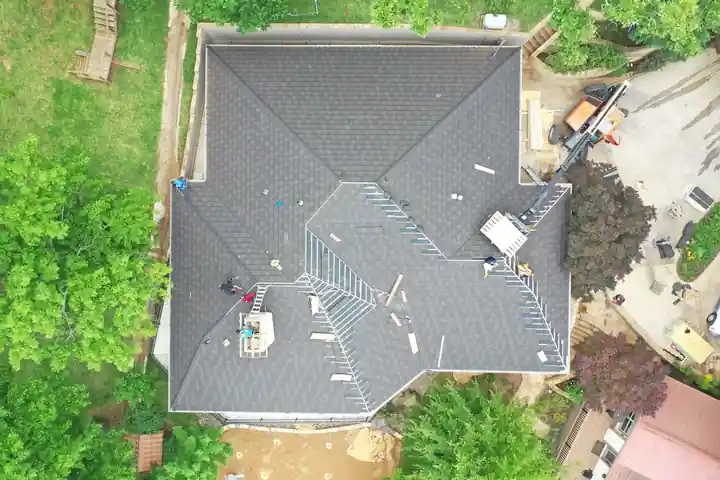 Overhead drone view of a BXC crew mid re-roof, new shingles laid over half the hip roof and bundles staged on the slopes