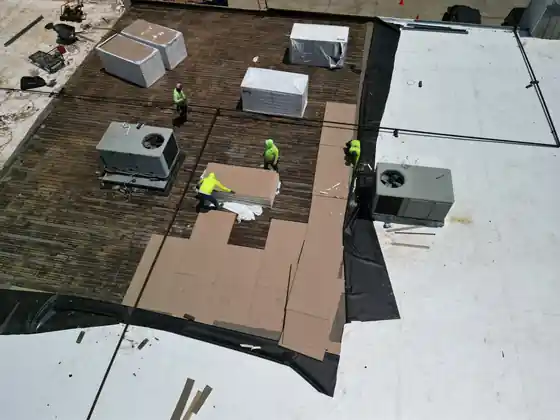 Commercial flat roof mid tear-off with rooftop HVAC units and a crew in hi-vis