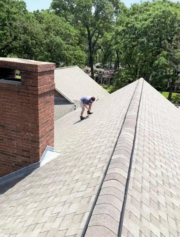A roofer working the ridge beside a brick chimney
