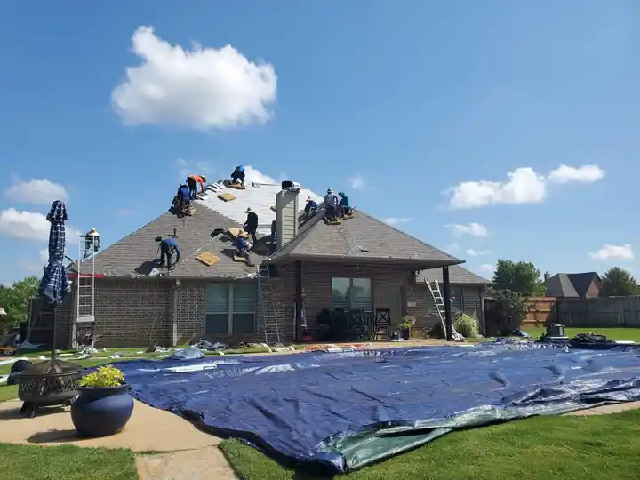 Crew on a brick home's roof with blue tarps protecting the lawn